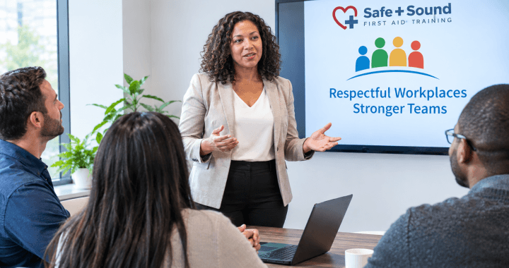 Workplace training session with a presenter speaking to employees while a screen displays the Safe + Sound First Aid Training logo and “Respectful Workplaces, Stronger Teams.”